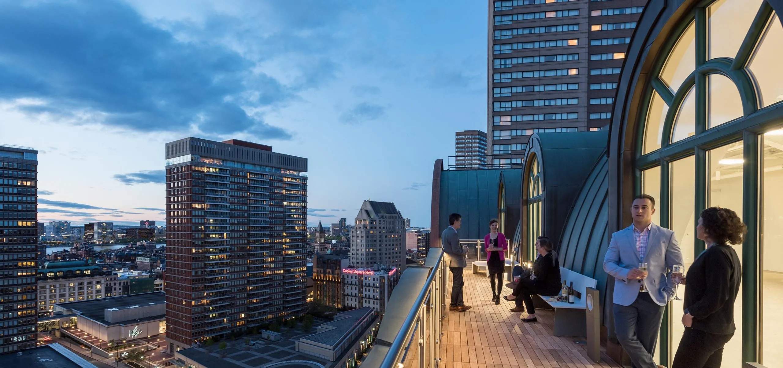 People sitting on balcony of office building with skyline in the background