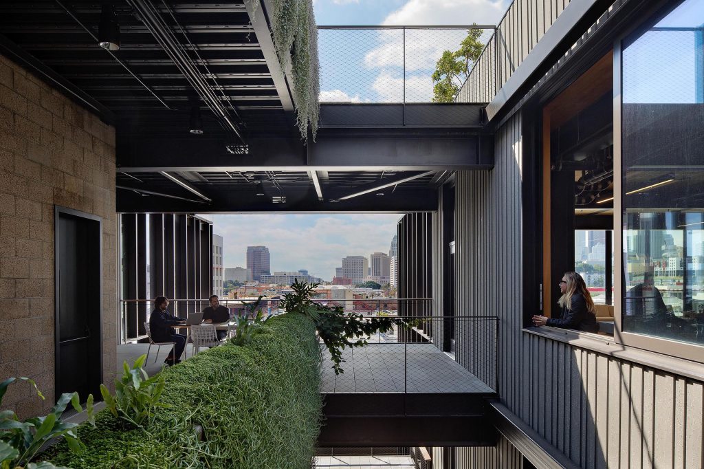 People sitting on multistory balcony with seating and at table and person looking out of large window