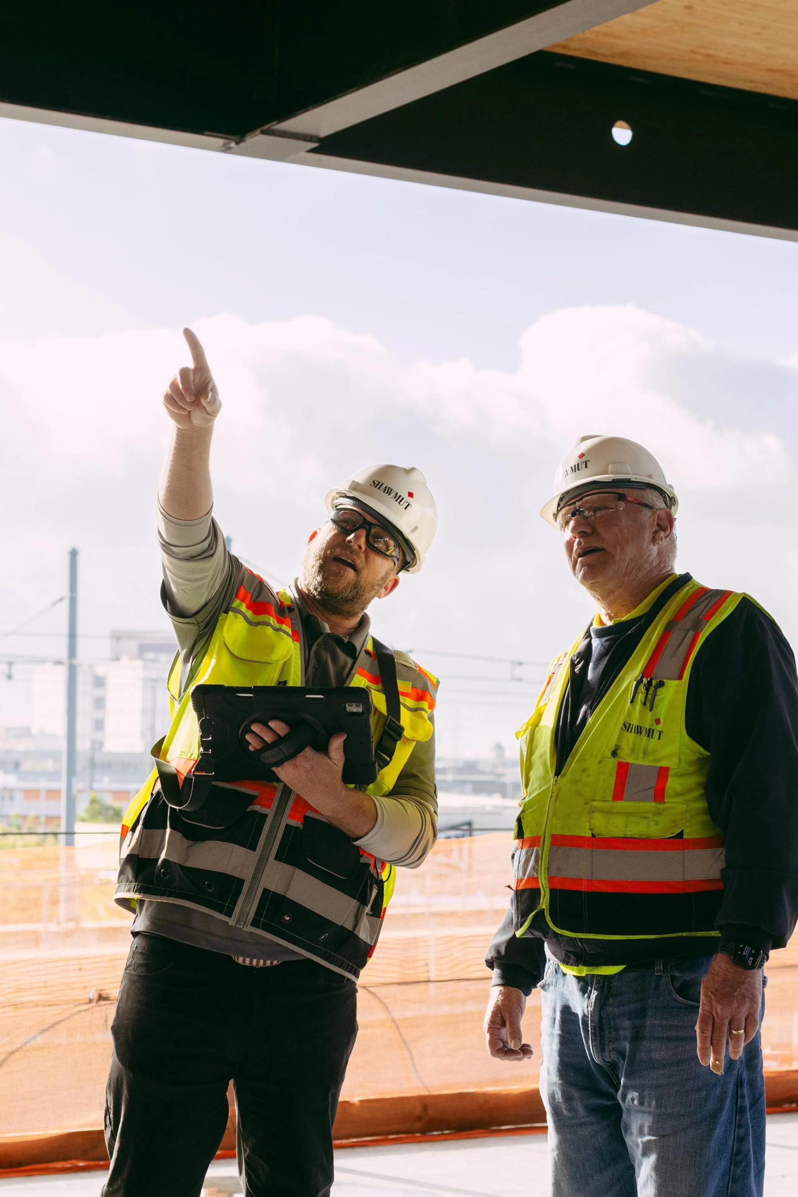 Two men in safety gear pointing at a part in a building