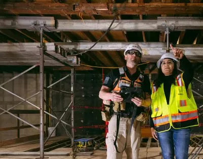 Two people in safety gear looking at support beams in buildings