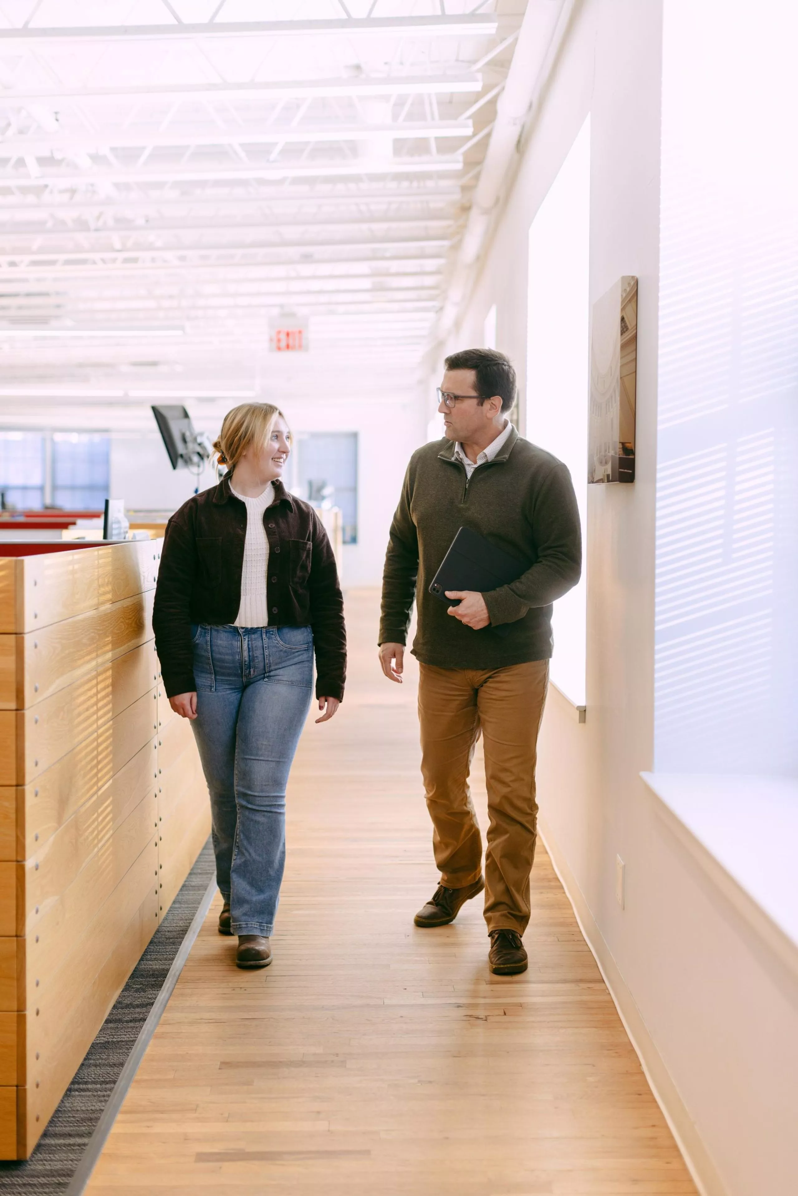 Two people walking down a hallway in an office and talking