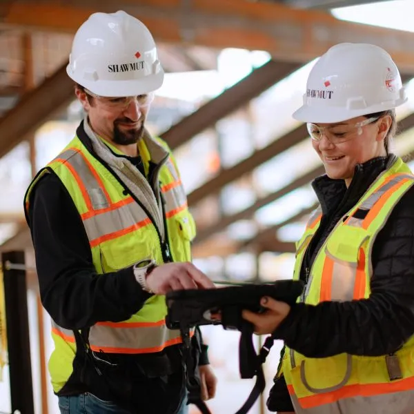 Two people in safety gear on construction site looking at tablet together