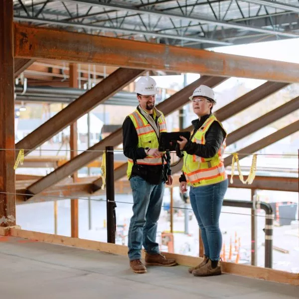 Two people in safety gear on construction site looking at tablet together