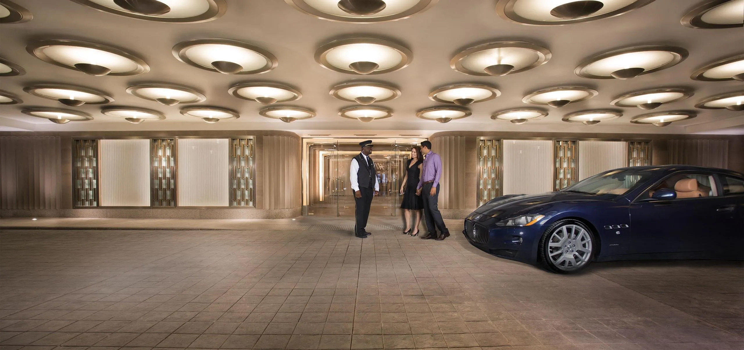 Front entrance of the Waldorf Astoria with three people and a car parked