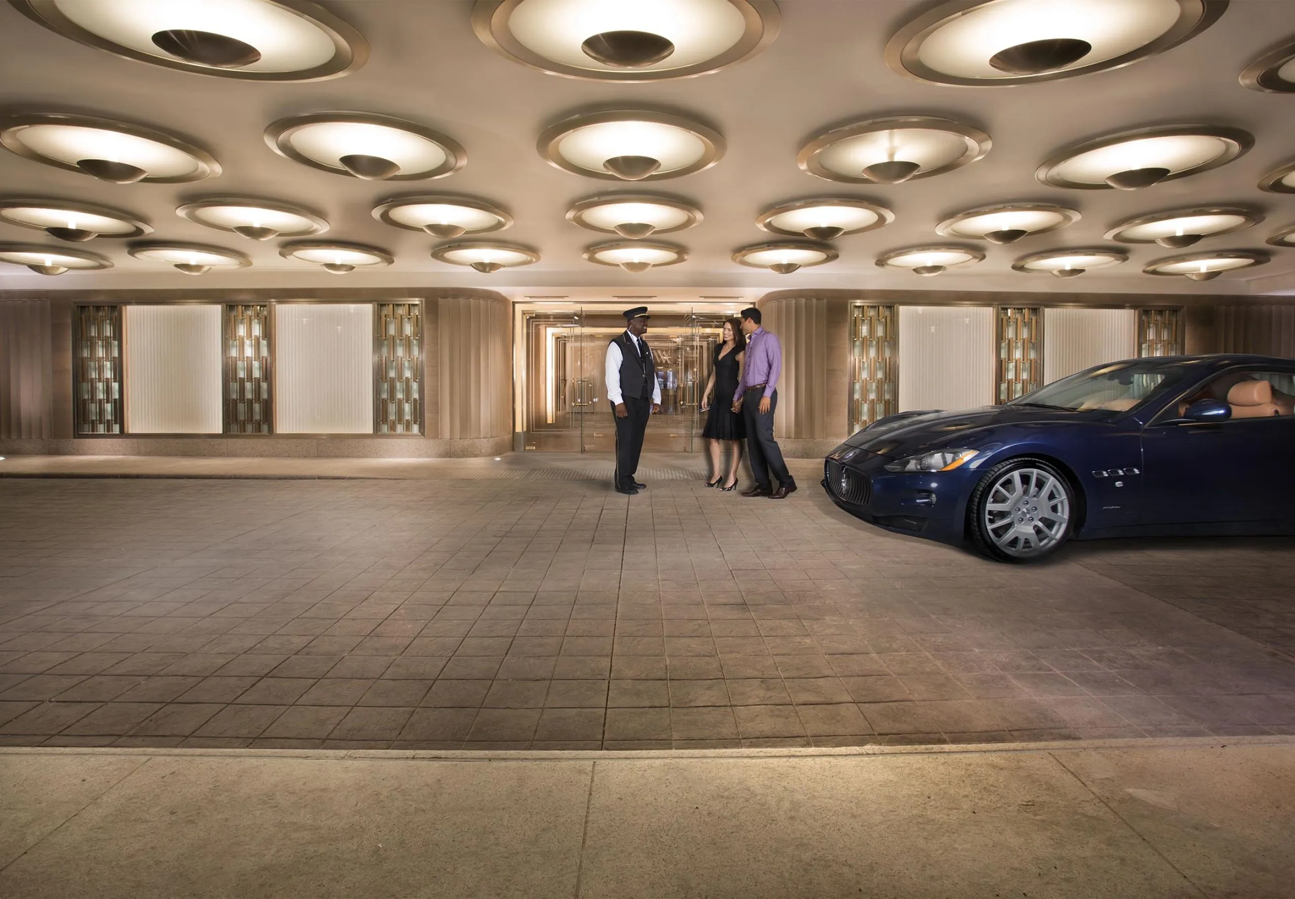 Front entrance of the Waldorf Astoria with three people and a car parked