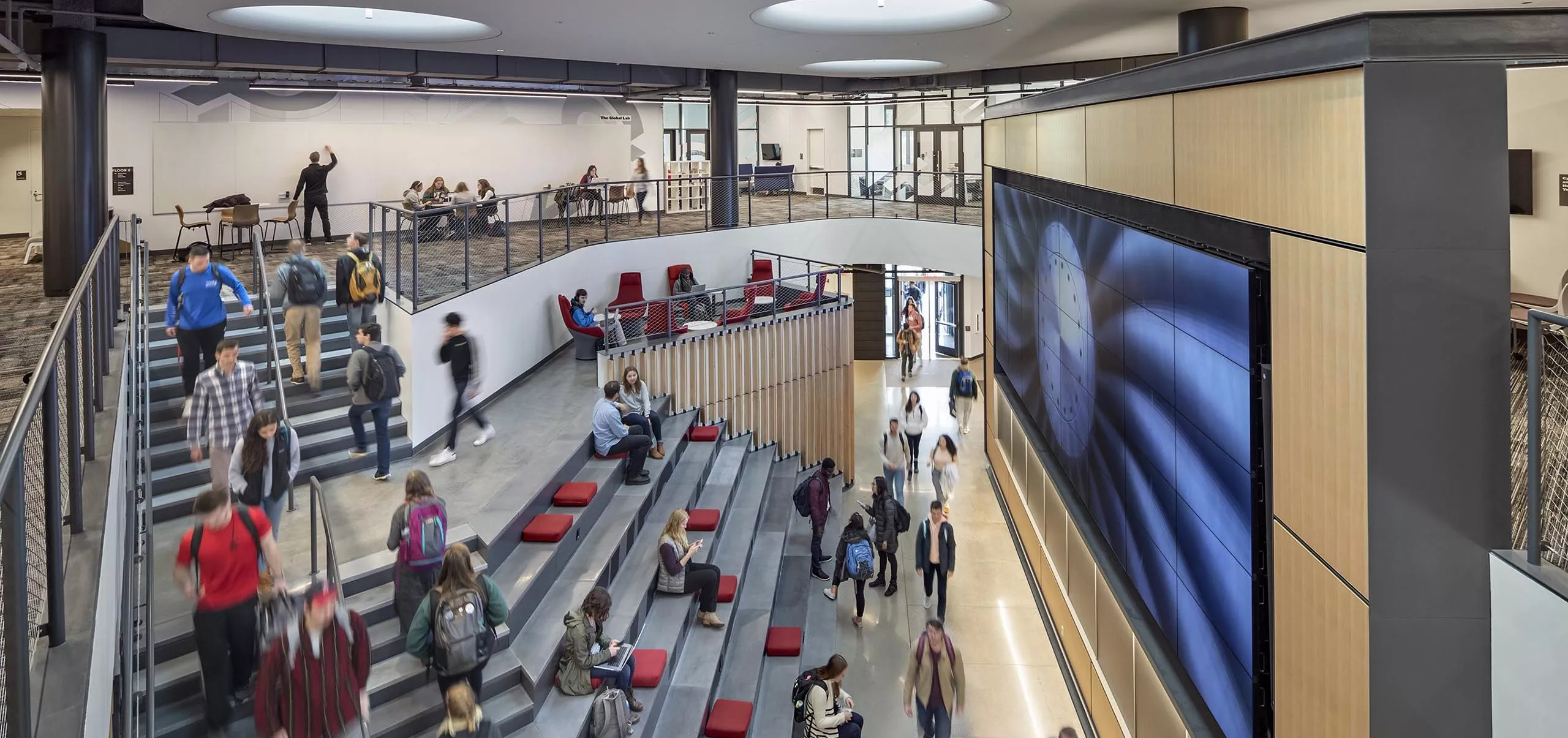 A group of people sitting on large stairs and walking in Innovation Studio & Messenger Residence Hall