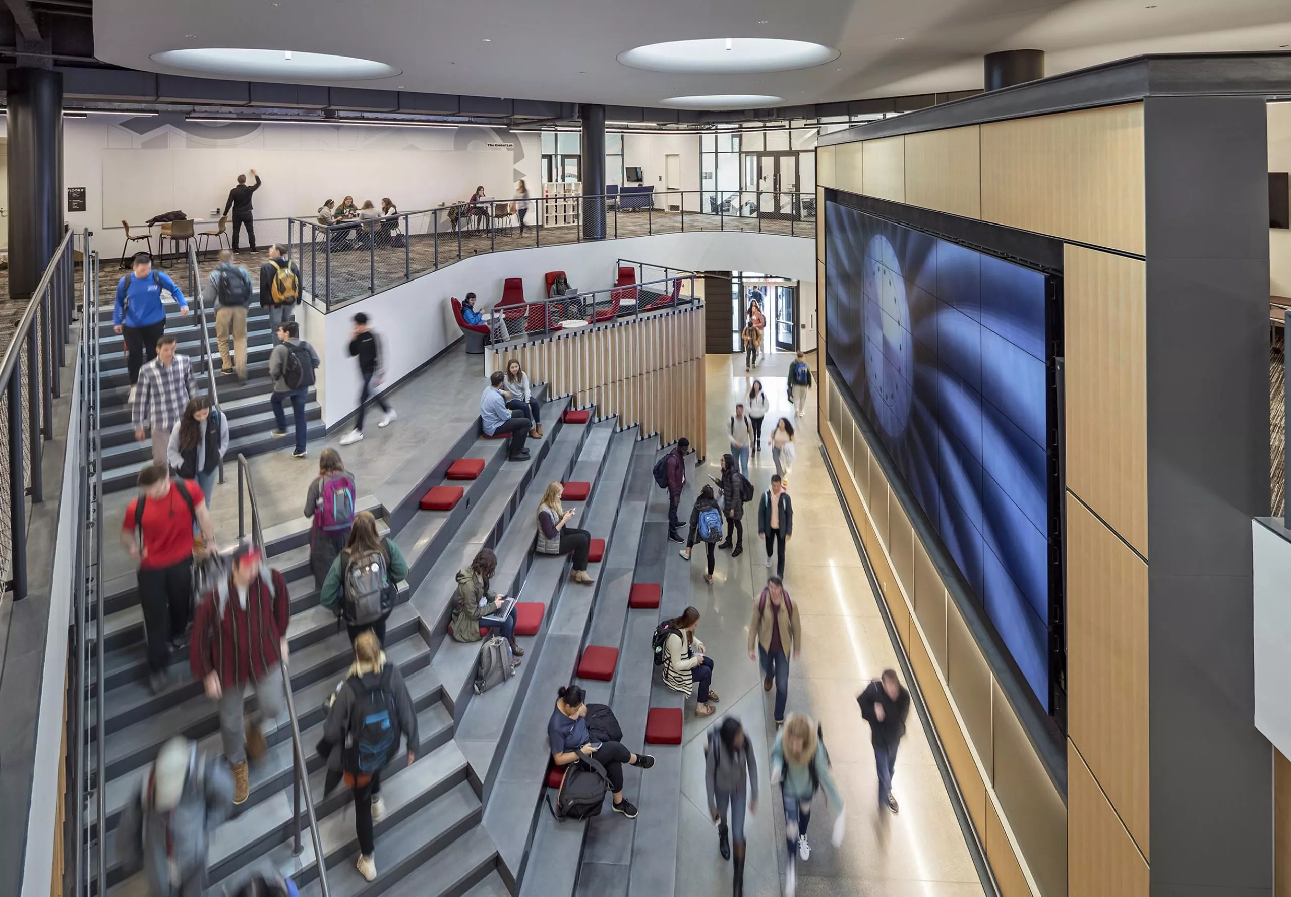 A group of people sitting on large stairs and walking in Innovation Studio & Messenger Residence Hall