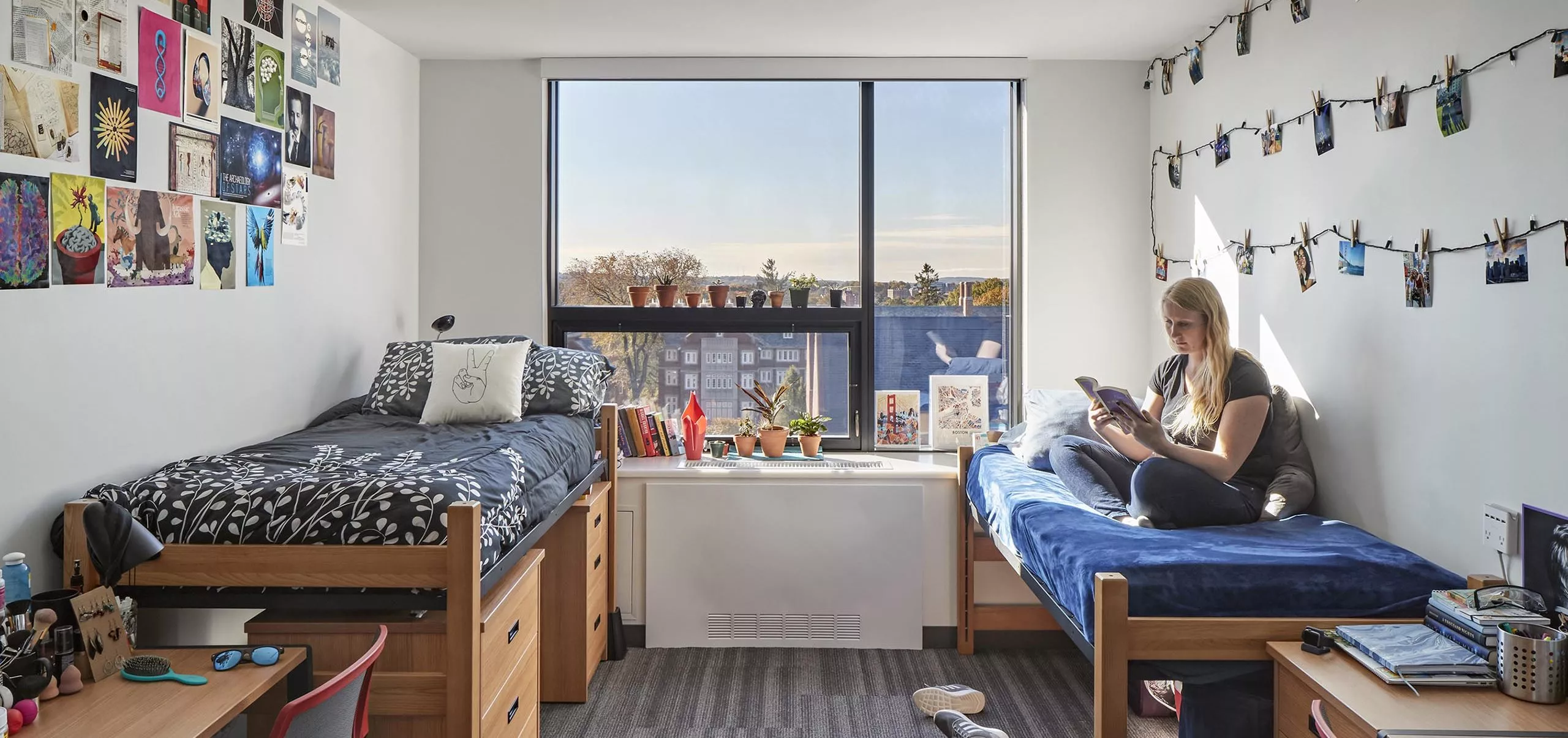 A woman sitting on a bed in a dorm room at Innovation Studio & Messenger Residence Hall