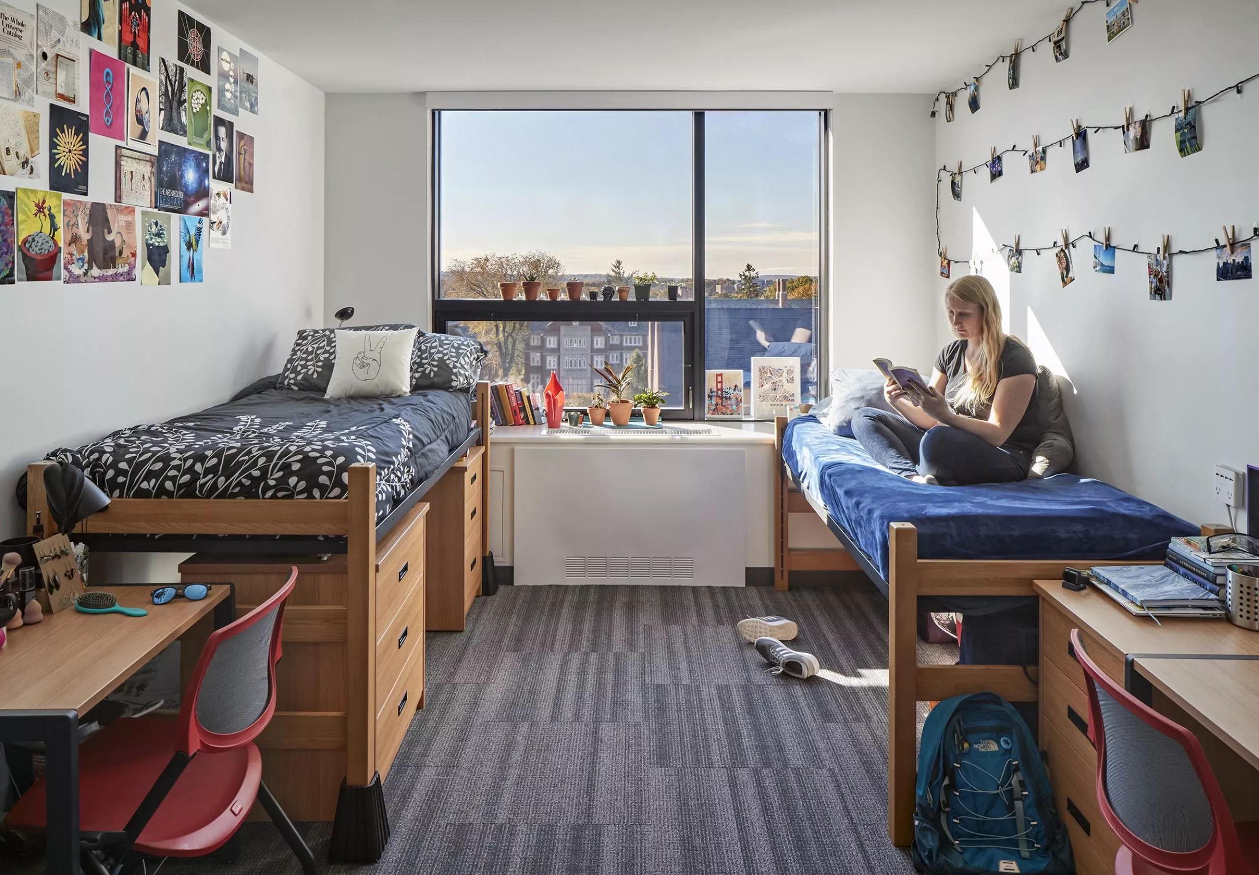 A woman sitting on a bed in a dorm room at Innovation Studio & Messenger Residence Hall